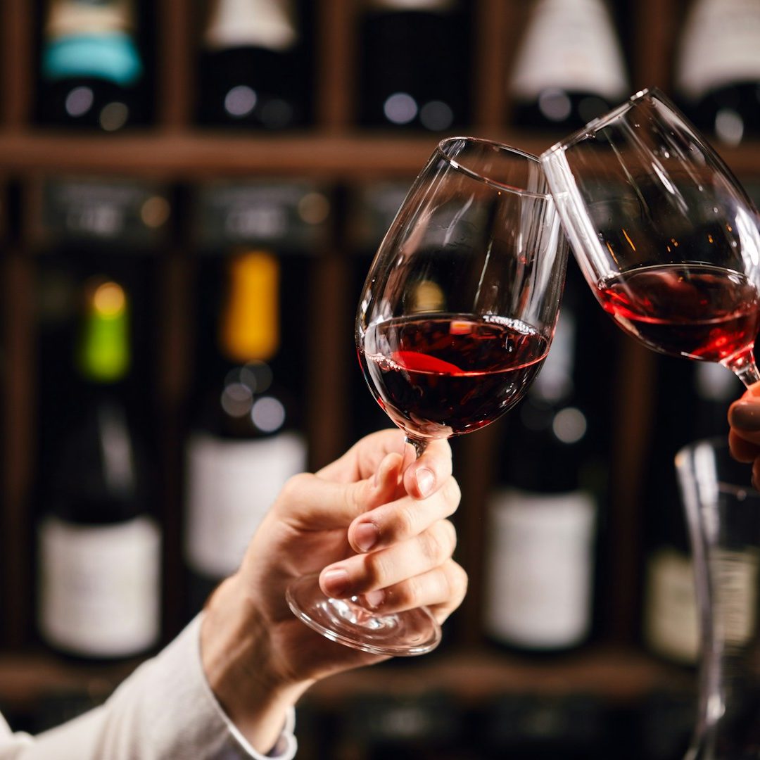 Weingläser mit Rotwein Weingläser prosten an, Rotwein, Weinregal im Hintergrund