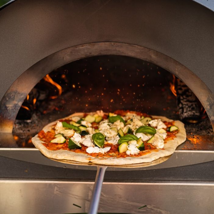 Pizza aus dem Holzsteinofen Pizza wird in den Holzsteinofen geschoben