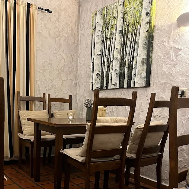 Innenbereich La Taverna Gütersloh Sitzbereich mit Holzstühlen und Tischen, Gemälde an Wand, Kerze auf dem Tisch